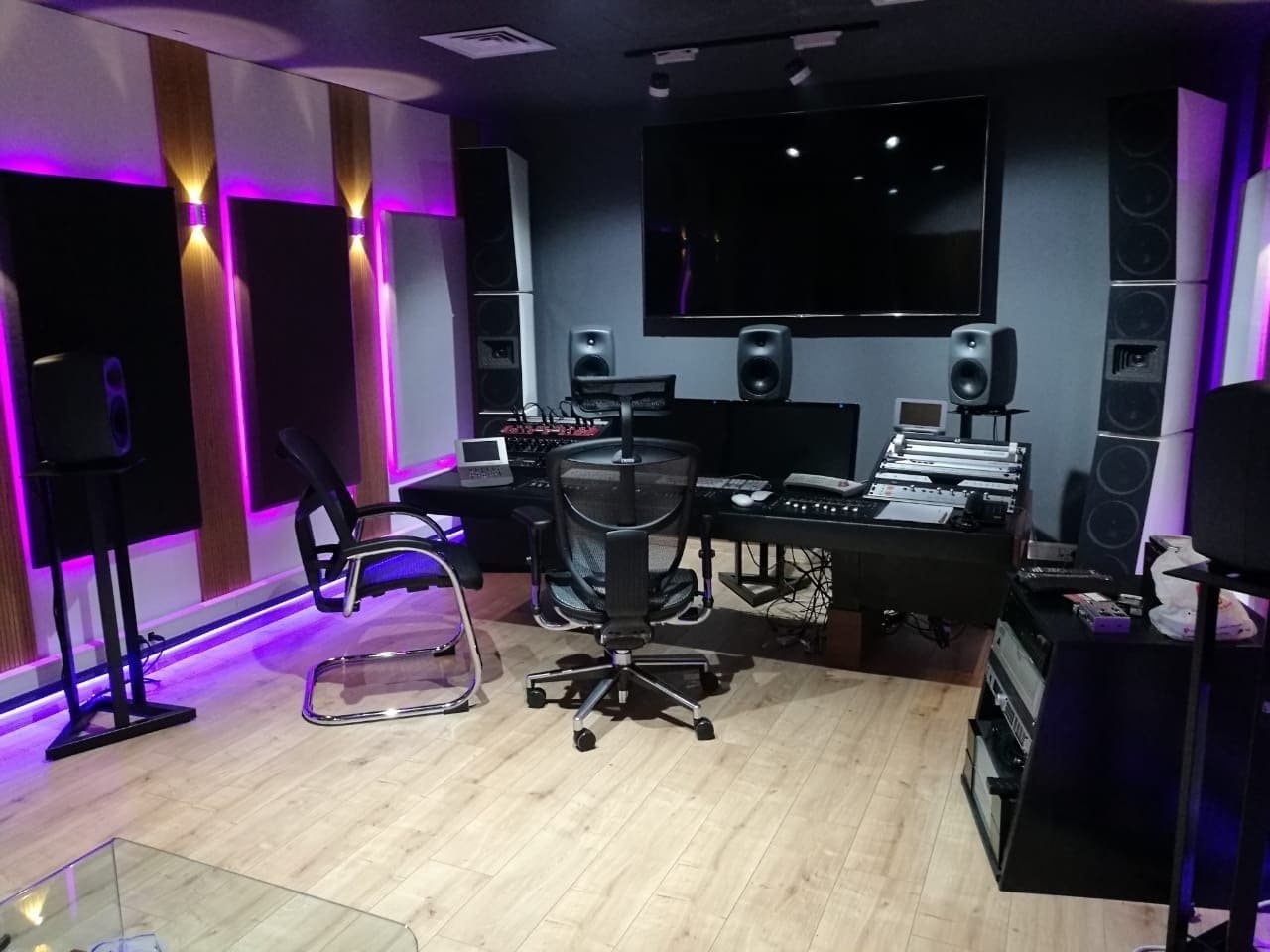 A mixing room with monitors and a control desk lit in purple